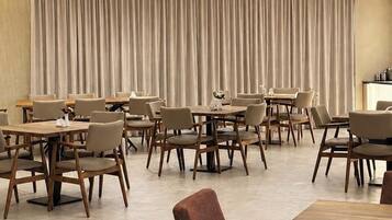 Un moderno comedor con varias mesas y sillas, un gran telón de fondo y luces empotradas en el techo.