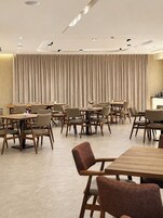 A modern dining area with multiple tables and chairs, a large curtain backdrop, and recessed ceiling lighting.