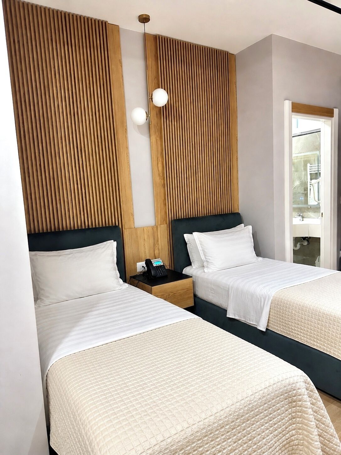 Ein Hotelzimmer mit zwei Betten, einer Wand mit Holzpaneelen, einem Nachttisch mit Telefon und einer Tür zu einem Badezimmer.