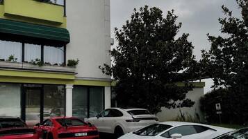 A hotel with a modern facade, a parking lot with several luxury cars, and a green awning over the entrance.