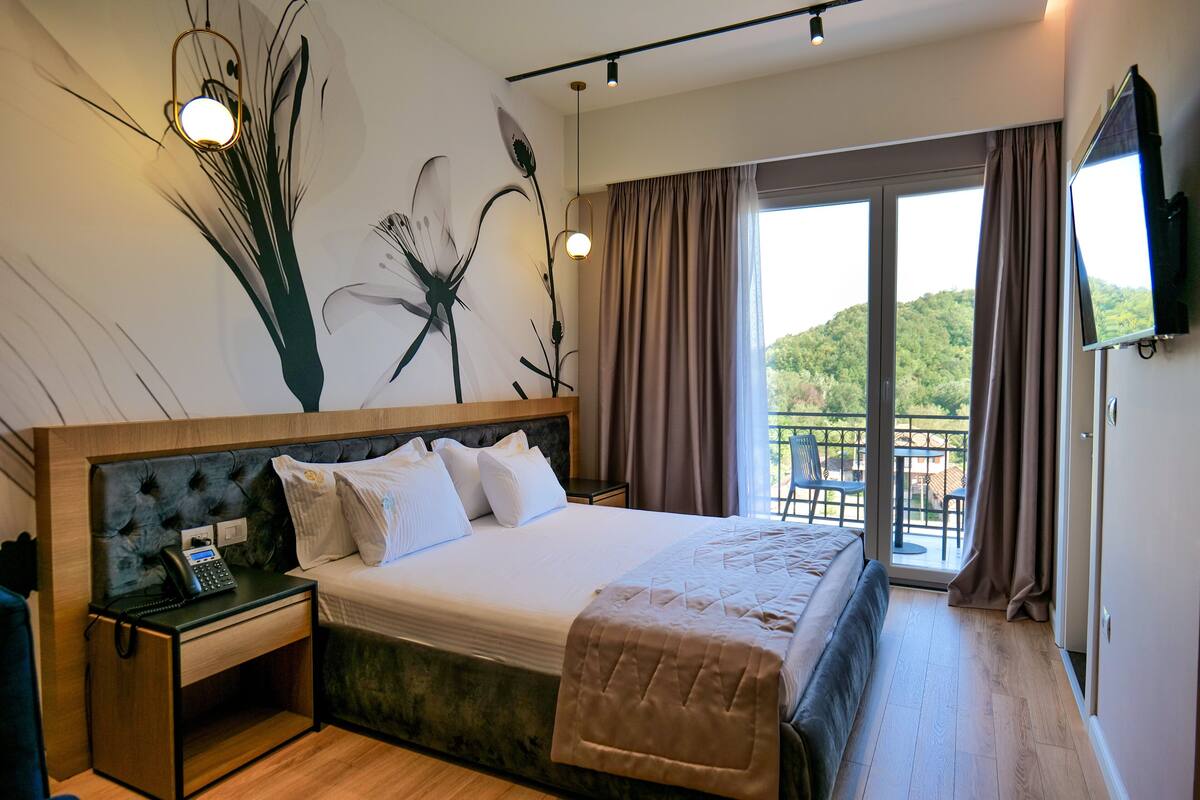 Een moderne hotelkamer met een groot bed, een bedtafeltelefoon, een flatscreen-tv en een balkon met uitzicht op de omgeving.