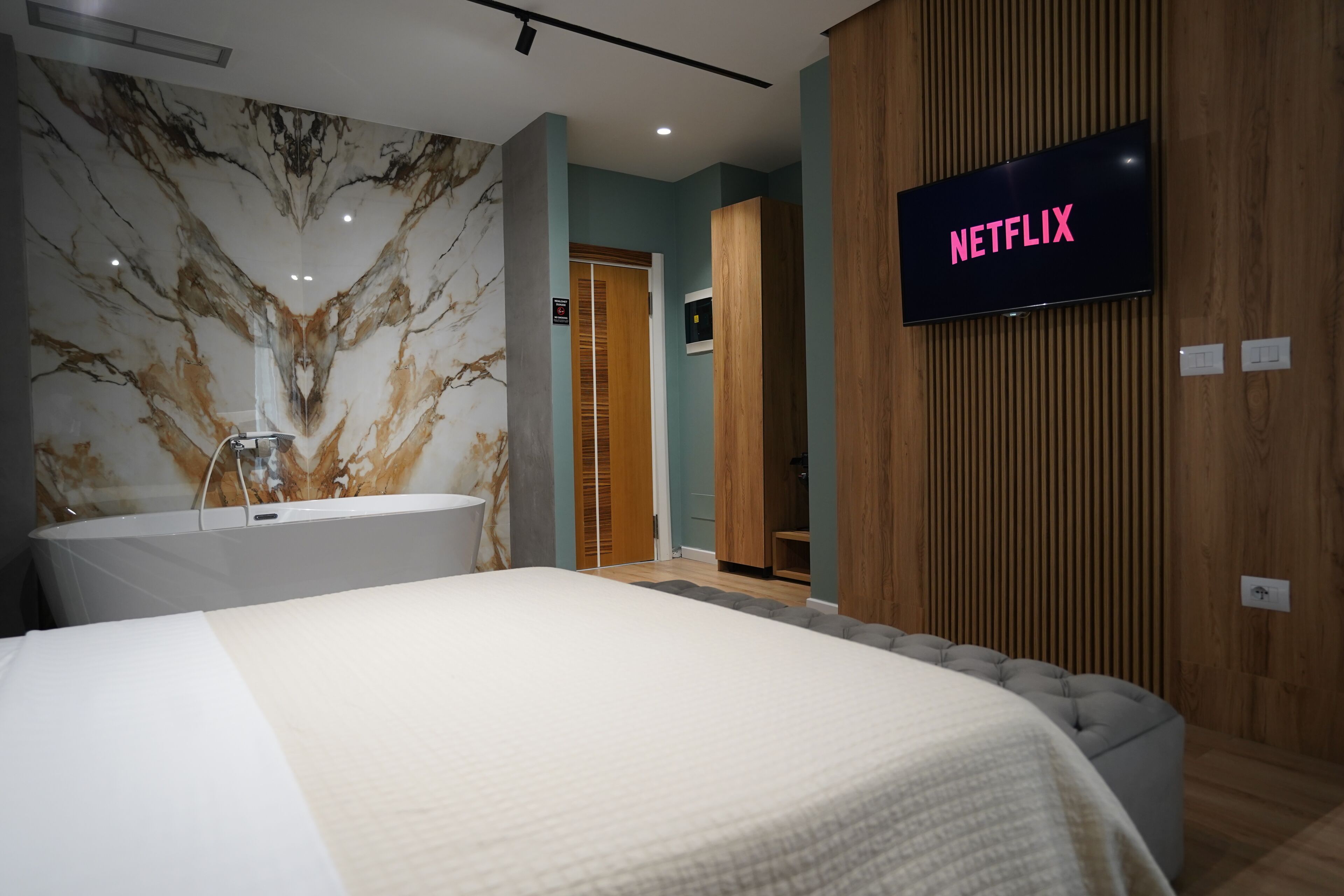 A modern hotel room with a large bed, a marble wall, a wooden panel wall, and a television displaying 'NETFLIX'.