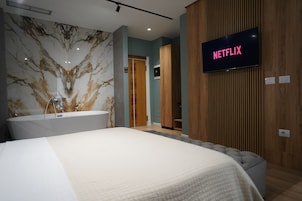 Una habitación de hotel moderna con una cama grande, una pared de mármol, un panel de pared de madera y un televisor mostrando 'NETFLIX'.