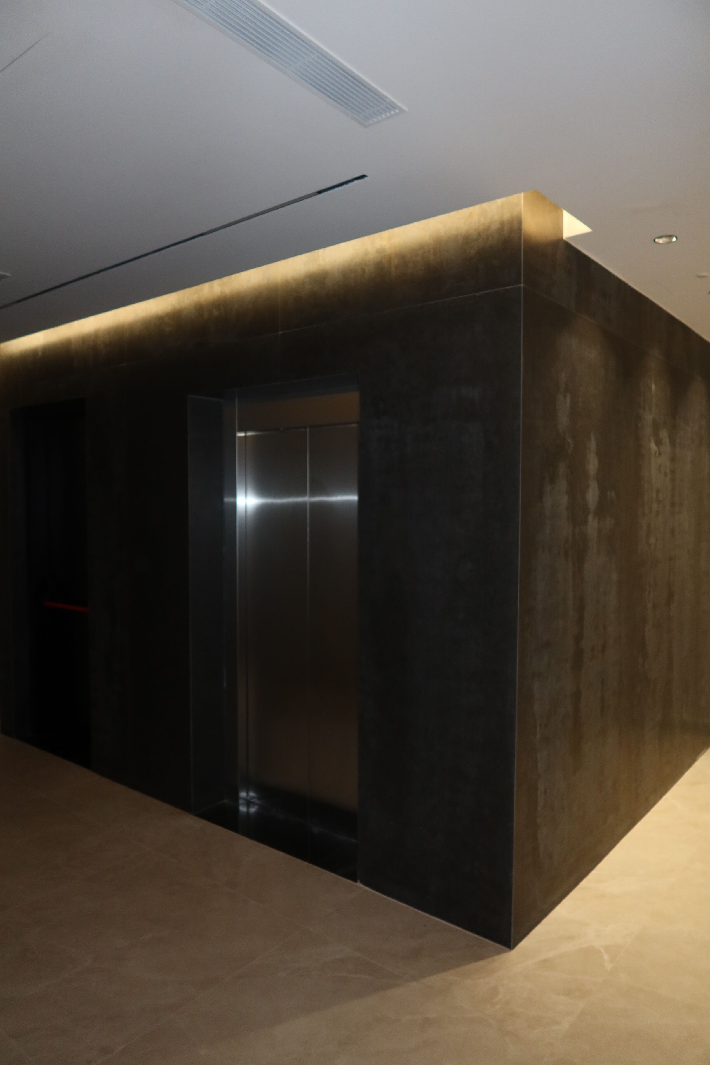 Un ascensor moderno con acabados metálicos, al lado de una pared con textura.