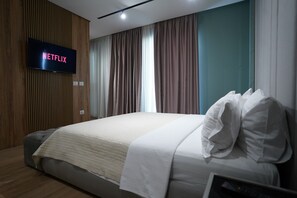 Une chambre d’hôtel moderne avec un grand lit, un téléviseur à écran plat fixé au mur et une fenêtre avec des rideaux.