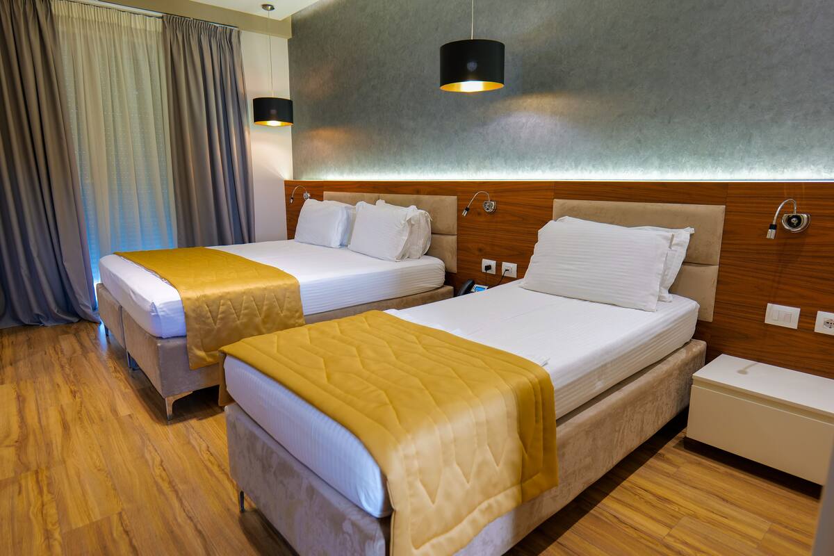 Een hotelkamer met twee bedden, houten vloeren, een hoofdbord met ingebouwde verlichting en een nachtkastje.