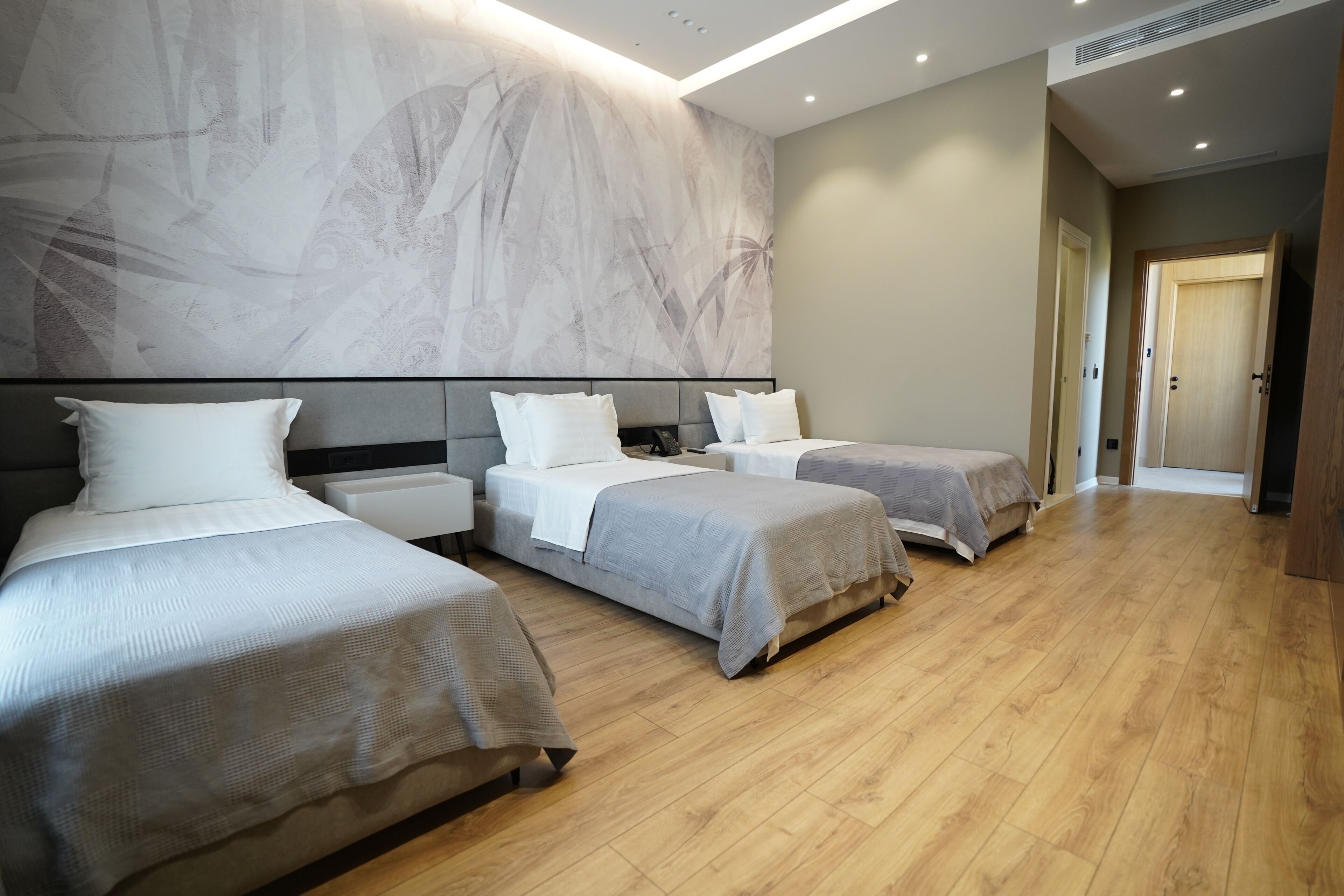 Habitación de hotel con tres camas, un amplio mural abstracto en la pared y suelo de madera.