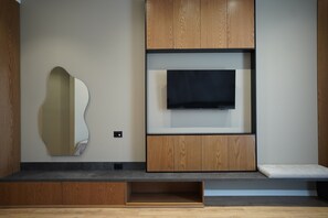 A modern living room with a flat-screen TV mounted on a wooden wall unit, a built-in bench, and a unique wall-mounted mirror. - Lord Hotel & Restaurant at AutoStation (Preze)