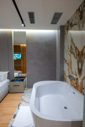 A modern bathroom with a large bathtub, a mirror, and a television in the background. - Lord Hotel & Restaurant at AutoStation (Preze)