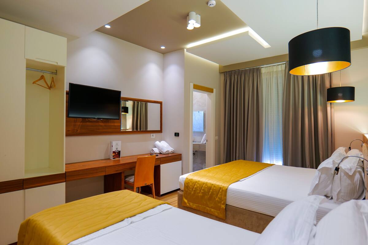 Een hotelkamer met twee bedden, een bureau, een stoel, een televisie en een badkamer die door een open deur zichtbaar is.