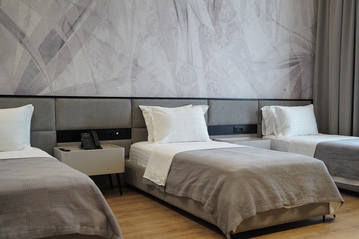 A hotel room with three beds, a bedside table with a phone, and a wall with a geometric pattern.