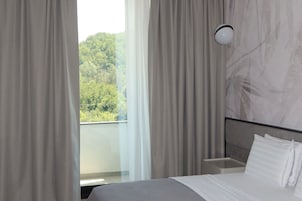 Habitación de hotel con cama, cortinas, mesita de noche y vistas a zonas verdes.