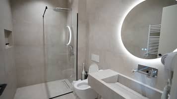 Un baño moderno con cabina de ducha de vidrio, inodoro y lavamanos con espejo.