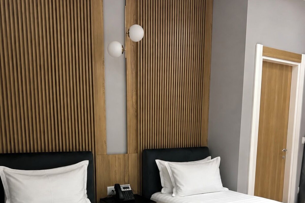 A hotel room with two beds, a wooden panel wall, a bedside table with a phone, and a door.
