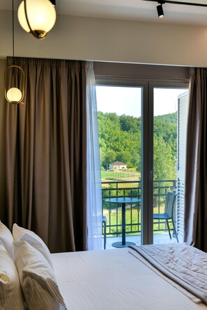 A hotel room with a bed, a balcony with a table and chairs, and a view of a green landscape. - Lord Hotel & Restaurant at AutoStation (Preze)
