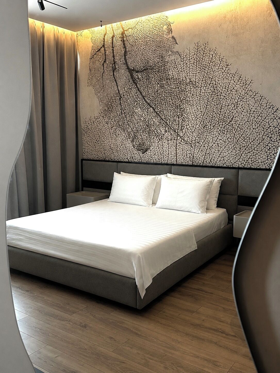 Un dormitorio moderno con una cama grande, un cabecero con diseño de árbol y suelo de madera.