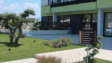 Placa de hotel com indicações para as instalações, incluindo restaurante, bar, piscina ao ar livre, parque infantil e aluguer de carros.