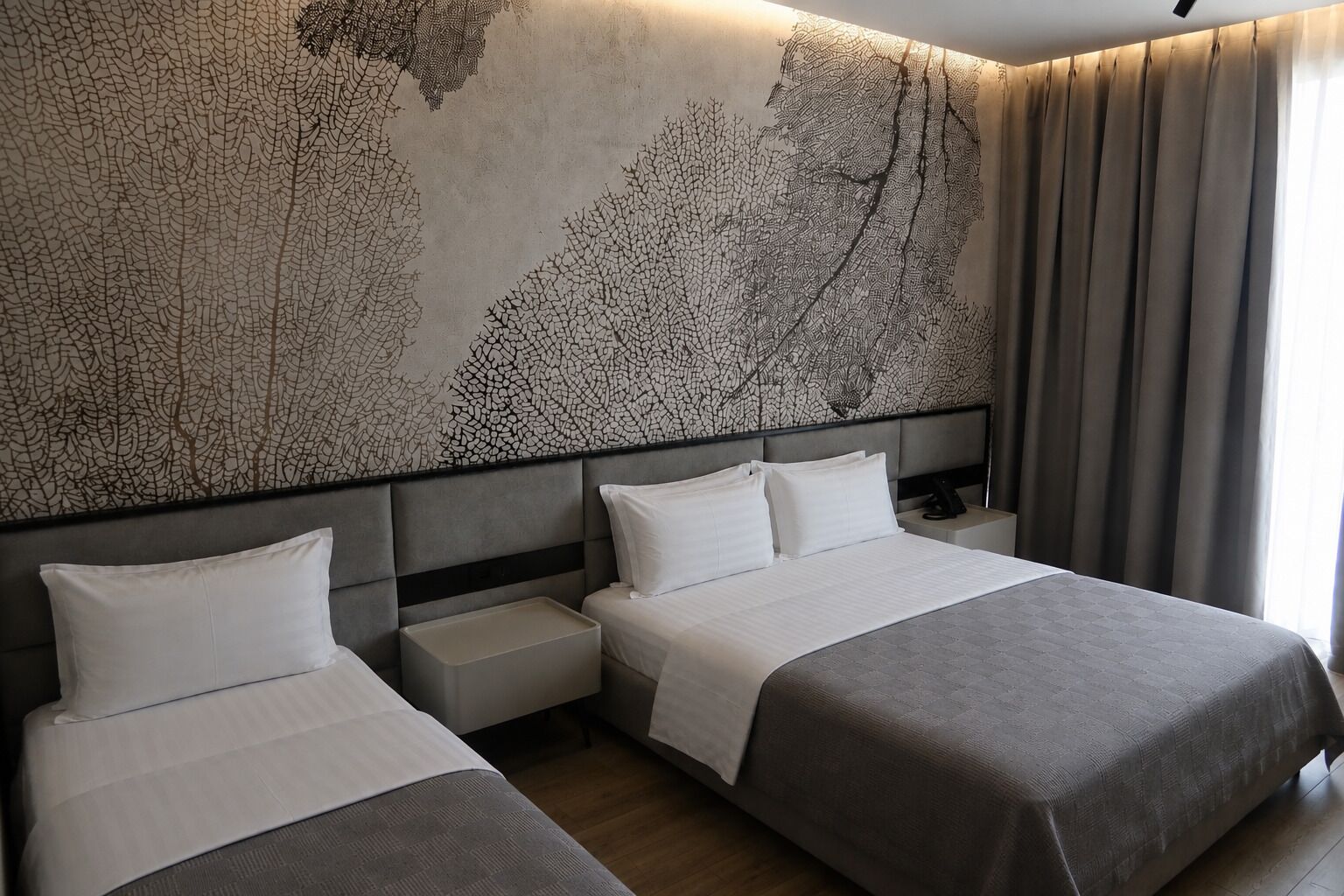 A hotel room with two beds, a large abstract wall art, a nightstand, and a window with curtains.
