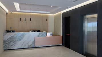 Zona de recepción de un hotel con mostrador de mármol, un escritorio de recepción, teléfono en la pared y un ascensor moderno.