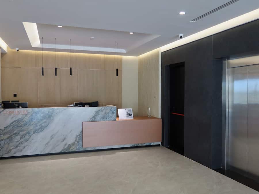 A hotel reception area with a marble counter, a reception desk, a wall-mounted phone, and a modern elevator.