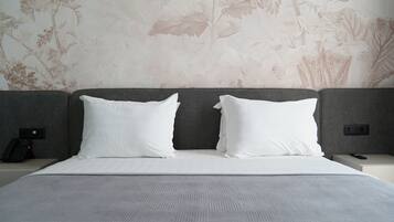 A hotel room with a large bed, two white pillows, a grey headboard, and a floral wallpaper.