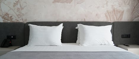 Habitación de hotel con una cama grande, dos almohadas blancas, un cabecero gris y papel tapiz floral.