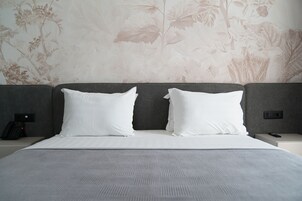 Habitación de hotel con una cama grande, dos almohadas blancas, un cabecero gris y papel tapiz floral.
