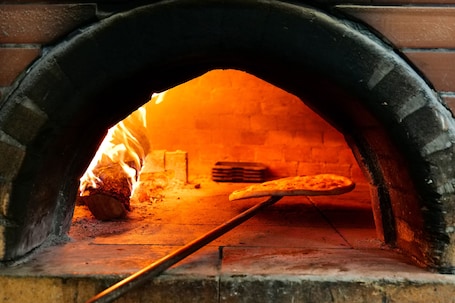 A brick oven pizza oven with a pizza being baked inside.