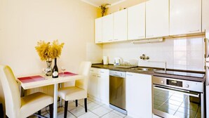 A compact kitchen with white cabinets, a dishwasher, an oven, and a dining table with chairs.