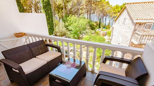A balcony with wicker furniture, a glass table, and a view of trees and buildings.