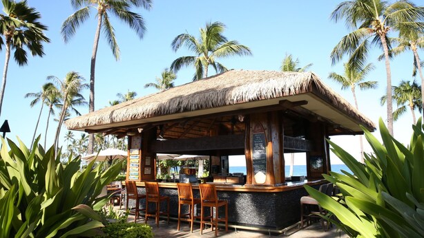 A thatched-roof bar with wooden chairs and a view of the ocean.