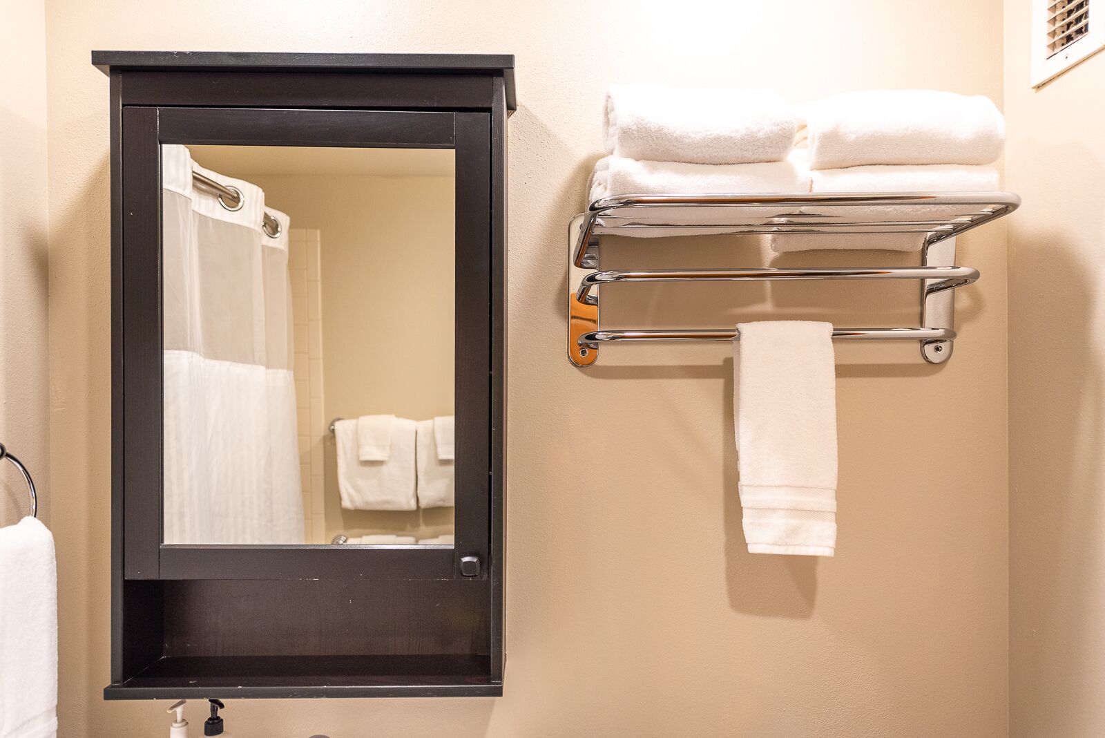 A bathroom with a mirror, a towel rack with folded towels, and a shower curtain.