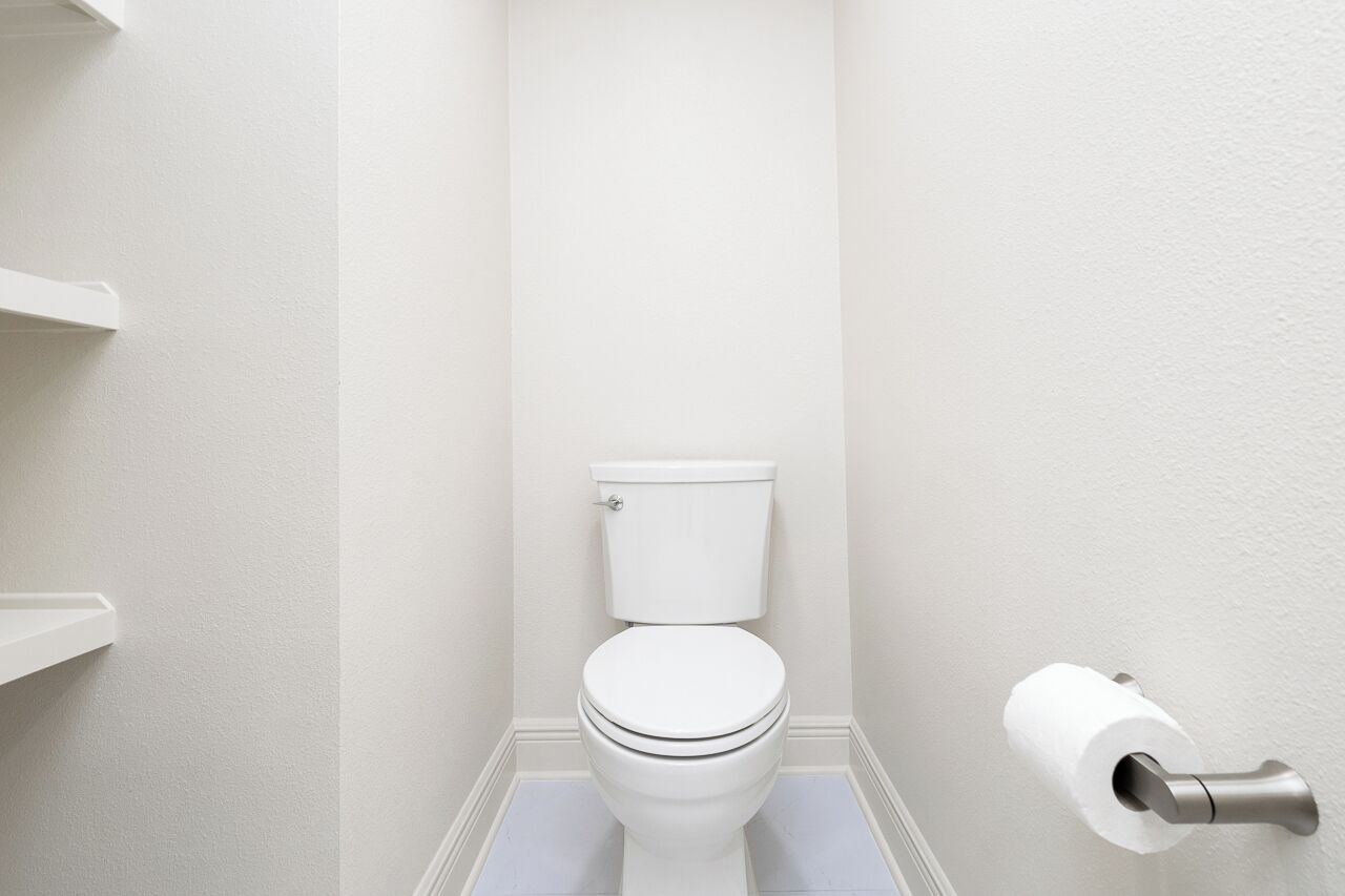 Des toilettes blanches avec une poignée de chasse d’eau, un porte-rouleau de papier toilette et un sol blanc.