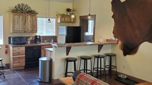 Una cocina amplia con armarios de madera, un refrigerador negro y una zona de comedor con un sofá y taburetes a cuadros.