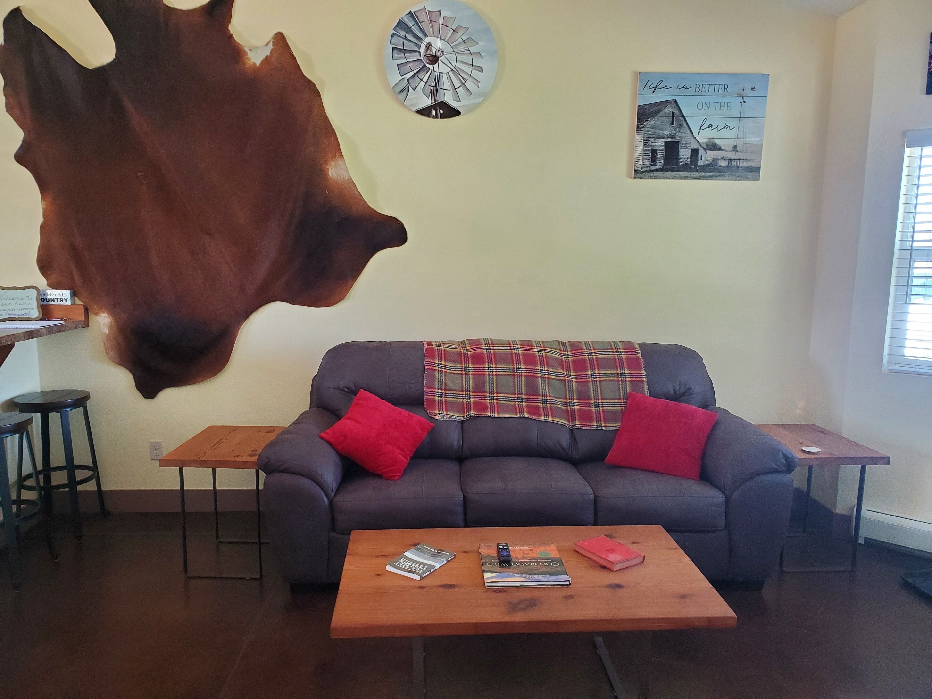 Ein Wohnzimmer mit einer Couch, einem Couchtisch mit Büchern, einer Wanduhr und einem aufgehängten Kuhfell.