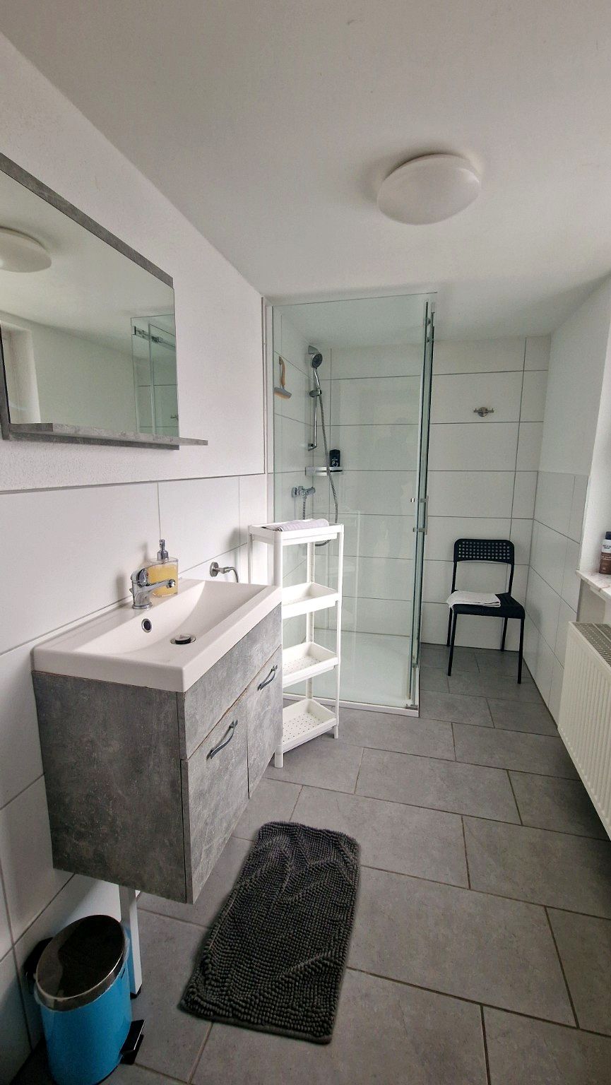 Une salle de bain moderne avec un meuble-lavabo, un miroir, une douche et une chaise.