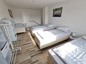 A room with three beds, a wooden floor, a door, and a wall-mounted picture. - New accommodation directly adjacent to Kassel (up to 18 pers.) (Kirchbauna)