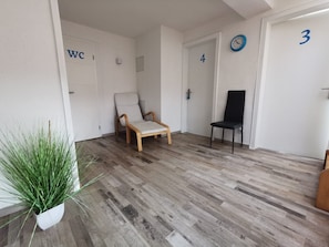 Una habitación con piso de madera, una silla blanca, una silla negra y una planta en maceta.