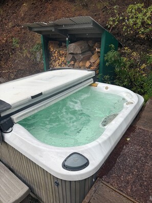 A hot tub with a wooden deck and a covered area with firewood. - Pet Friendly Quiet Cabin with Privacy, Hot Tub, and Backcountry Access. (Ketchum)