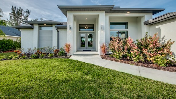 A modern two-story house with a front entrance, a covered porch, and a well-maintained lawn. - Stunning! Private Villa with pool, for families. No storm damage.  (Cape Coral)