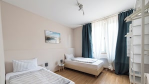 Une chambre avec deux lits, une table de chevet, une lampe, une fenêtre avec des rideaux et un tableau au mur.