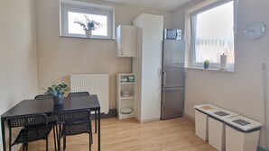 Une cuisine compacte comprenant un réfrigérateur, une table à manger avec des chaises, un radiateur et une fenêtre avec une horloge.