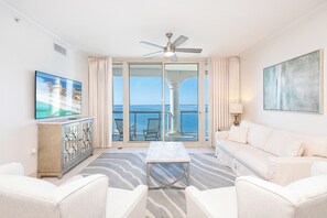 Relax in this stylish living room with a large flat-screen TV, comfortable sofa and armchair, and sliding glass door leading to a balcony with ocean views.