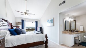 A bedroom with a bed, a desk, a vanity with a mirror, and a ceiling fan.