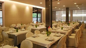 Une salle de banquet avec de nombreuses tables dressées pour le repas, chacune étant recouverte d’une nappe blanche et agrémentée de chaises assorties.