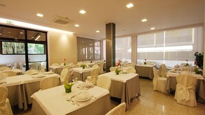 Une salle de banquet avec de nombreuses tables rondes, chacune recouverte d’une nappe blanche et mise avec des assiettes et des couverts.