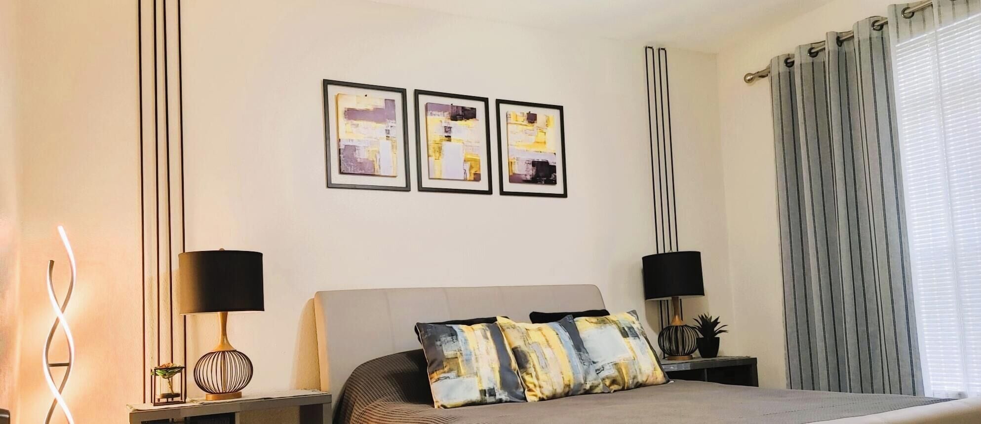 Een slaapkamer met een bed, twee nachtkastjes, een wandlamp, een potplant en een raam met gordijnen.