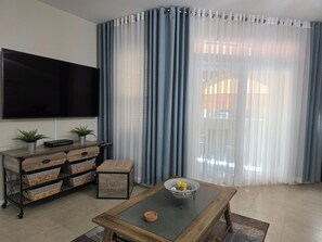 Un salón con televisión de pantalla plana, una mesa de centro de madera con un cuenco, una mesita auxiliar y un mueble con cestas.