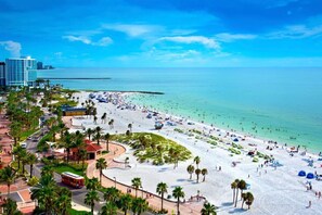 Una playa con palmeras, un paseo marítimo y un edificio grande al fondo.