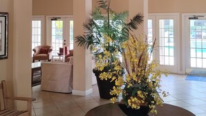 Un interior espacioso con una mesa redonda de madera, una araña y una gran maceta con flores amarillas.